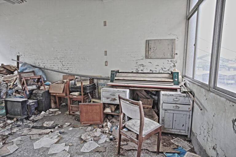 A derelict commercial office space in London filled with trash, broken furniture, and debris following a successful squatter eviction.