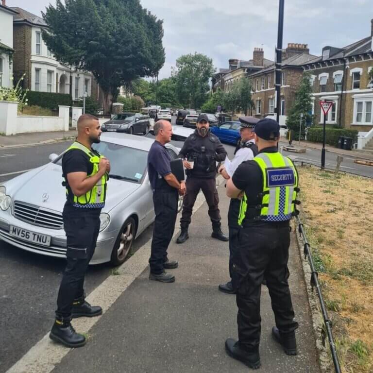 Security enforcement officers in high-visibility vests conducting a residential patrol and speaking with local residents.